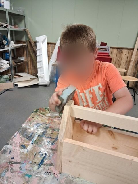 Een jongen timmert aan een houten kist